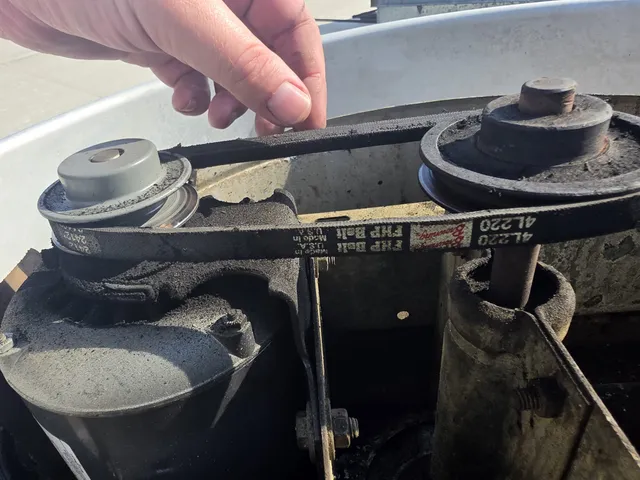 Technician inspecting a rooftop exhaust fan belt during a repair visit
